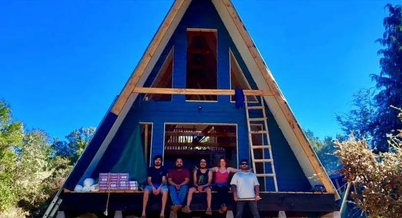 El equipo SLAICO sentado en el frente de una casa alpina azul en construcción